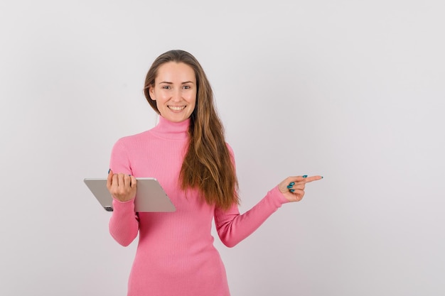 A jovem sorridente com computador tablet está apontando para a direita no fundo branco