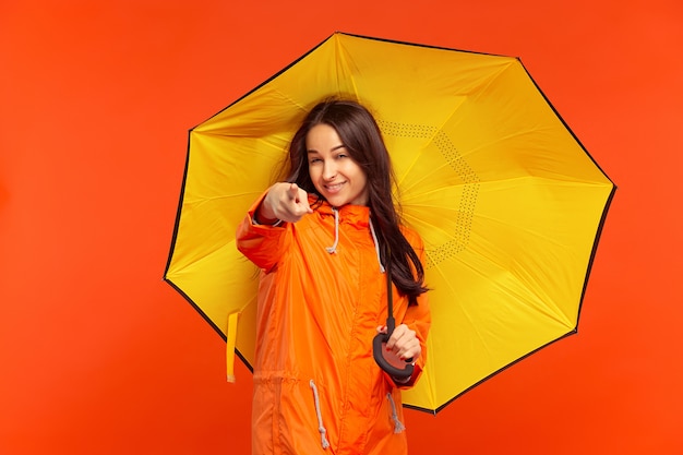 Foto grátis a jovem sorridente e feliz posando no estúdio com uma jaqueta laranja outono e apontando para a frente, isolada na parede laranja