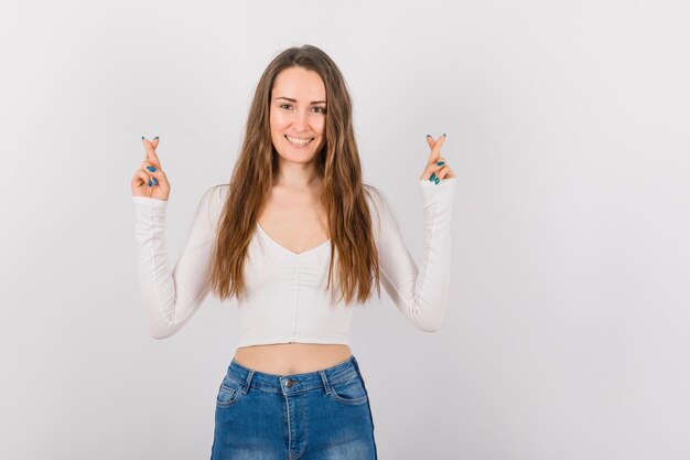 A jovem sorridente está levantando as mãos cruzando os dedos no fundo branco