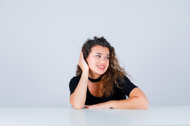 A jovem sorridente está olhando bem, segurando a mão atrás da cabeça no fundo branco