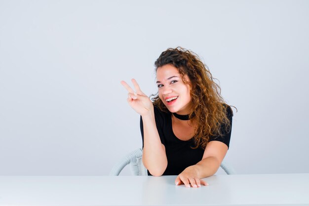 A jovem sorridente está olhando para a câmera mostrando dois gestos no fundo branco