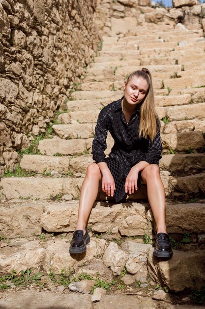 A loira olha para a esquerda de vestido preto sobre fundo de pedra