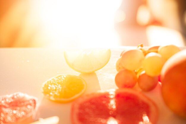 A luz do sol caindo sobre as fatias de limão; laranja; toranja e uvas na superfície