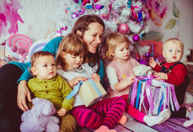 A mãe abraça seus filhos perto da Árvore de Natal