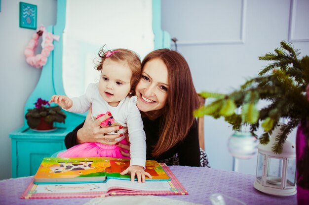 A mãe alegre abraça atrás de sua filha pequena sentada em