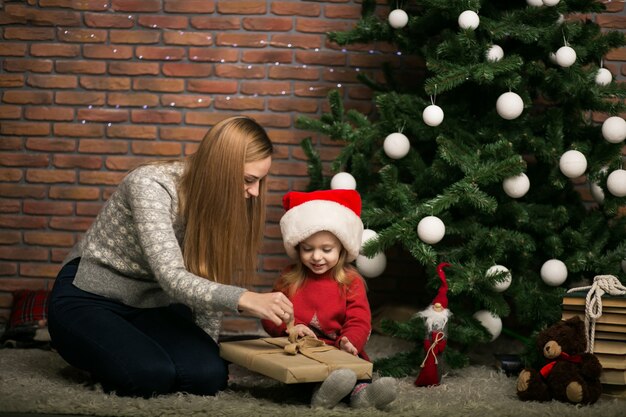 A mãe e a filha embalam presentes pela árvore de Natal