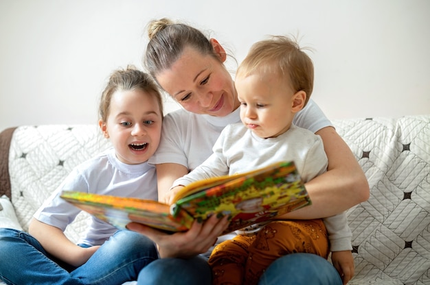 Foto grátis a mãe e seus dois filhos estão lendo um livro em casa no sofá. feliz e sorridente