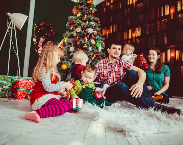 A mãe, pai e filhos sentados perto da árvore de natal
