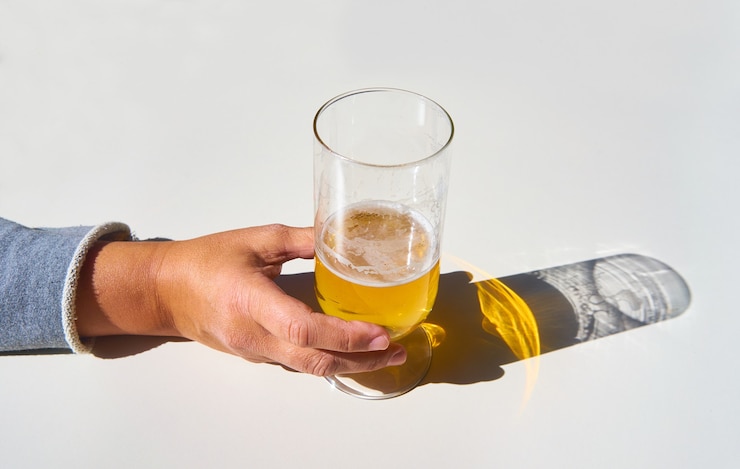 Foto grátis a mão da fêmea pega um copo de cerveja com a sombra refletida na mesa branca