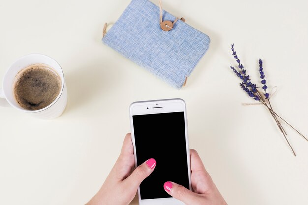 A mão da mulher que guarda o telefone celular com copo de café; diário e lavanda no fundo