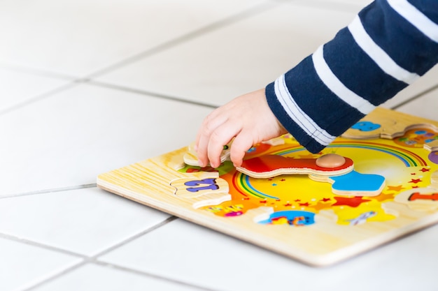 A mão de uma criança brincando com um quebra-cabeça de relógio de madeira em foco suave