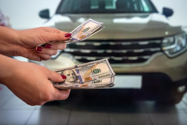 A mão do belo homem saudável segura uma soma redonda de notas de dólar perto de novos carros caros em um showroom de carros. conceito de negócios. o conceito de escolha