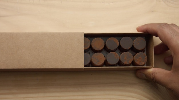 Foto grátis a mão do homem abre uma caixa de artesanato de doces de chocolate na mesa de madeira