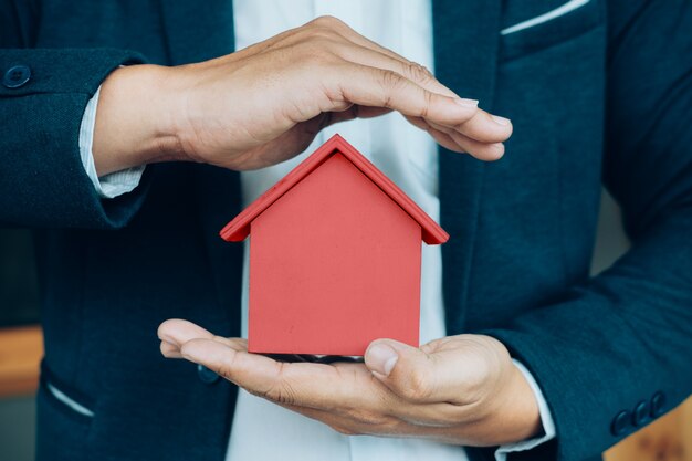 A mão do homem de negócios segura o modelo da casa que poupa uma pequena casa.