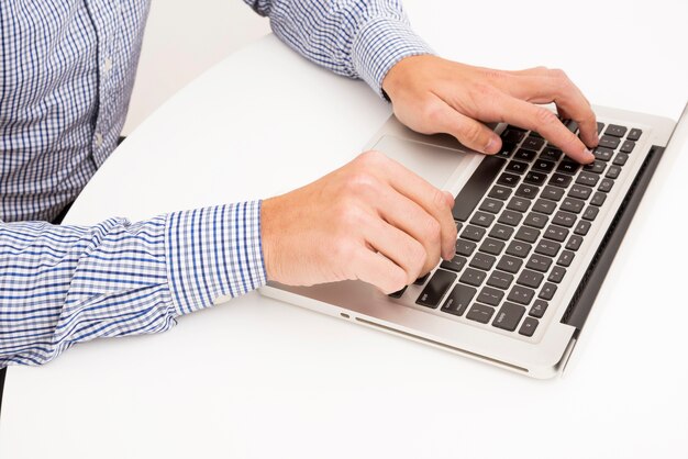 A mão do homem digitando no laptop sobre a mesa branca