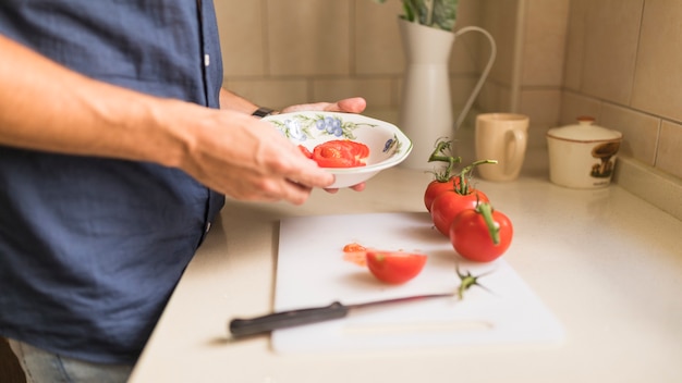 A mão do homem segurando a fatia de tomate na tigela