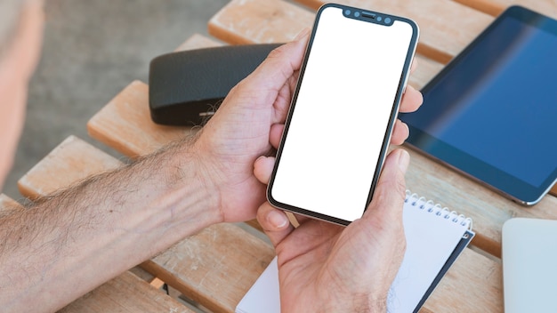 A mão do homem segurando o smartphone com tela branca em branco na mesa de madeira