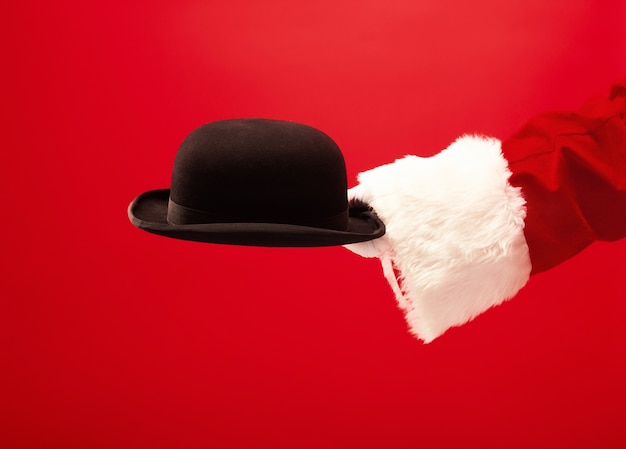 A mão do Papai Noel segurando um chapéu preto no vermelho