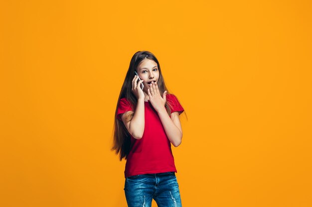 A menina adolescente feliz que está e que sorri contra o espaço alaranjado.