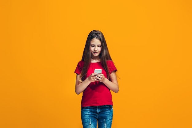 A menina adolescente feliz que está e que sorri contra o espaço alaranjado.