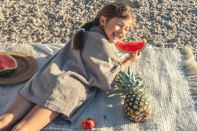 A menina come fruta deitada em um cobertor na praia
