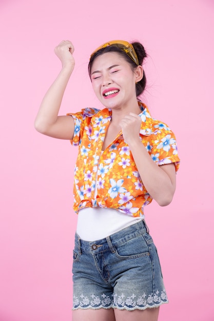 A menina da forma veste-se acima com gestos de mão em um fundo cor-de-rosa.