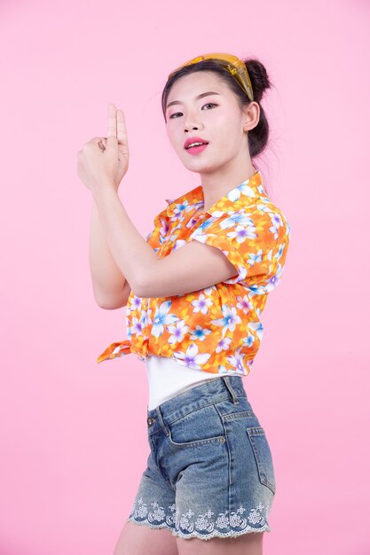 A menina da forma veste-se acima com gestos de mão em um fundo cor-de-rosa.