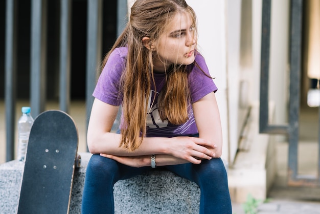 A menina do skater senta com seu skate mordendo o lábio