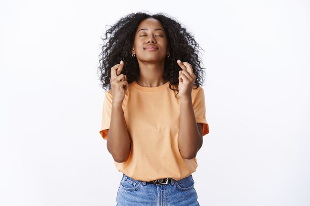 A menina espera que Deus ouça orações, tornando o desejo desejo em realidade. Esperançosa e atraente jovem aluna deseja passar nos exames da universidade fechar os olhos, levantar a cabeça, cruzar os dedos, boa sorte, parede branca