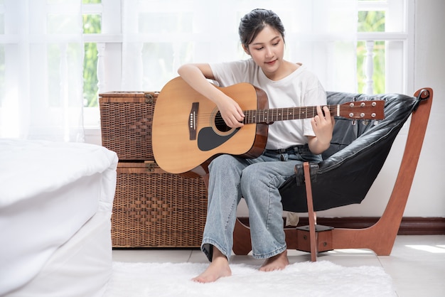 A menina está sentada e tocando violão na cadeira.