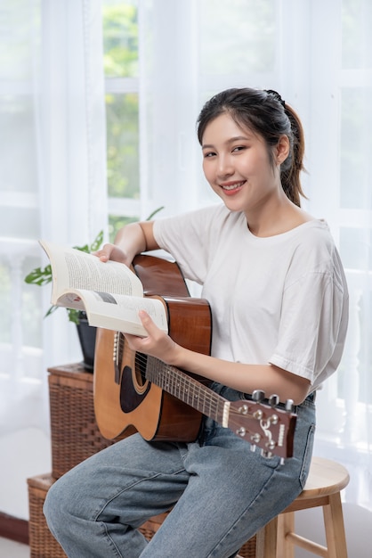 A menina está sentada e tocando violão na cadeira.