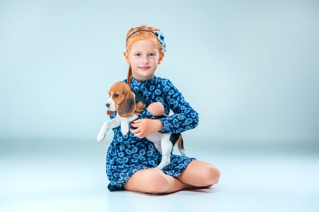 A menina feliz e um cachorro beagle na parede cinza