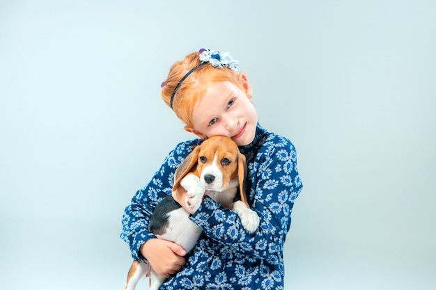 A menina feliz e um filhote de cachorro beagle na parede cinza