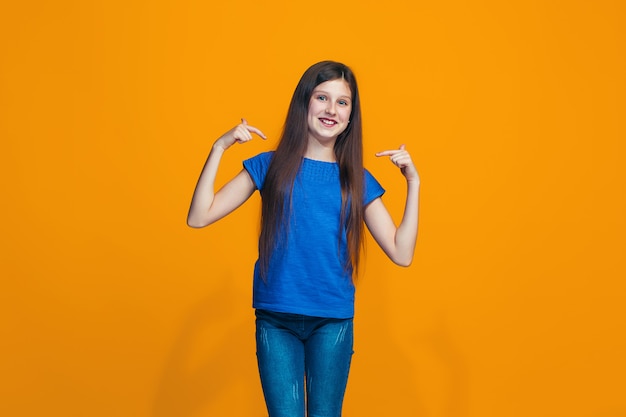 A menina feliz em pé e sorrindo contra a parede laranja