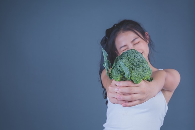 A menina prende os vegetais em um fundo cinzento.