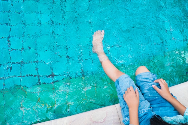 A menina relaxa os pés com água na piscina.