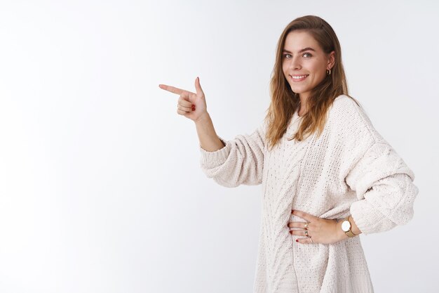 A menina sabe onde vamos. Foto de perfil linda mulher de aparência amigável ajuda a escolher o caminho apontando para o lado virando a câmera olhando para você sugerindo direção em pé sorrindo fundo branco feliz casual