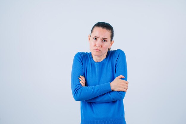 A menina triste está se abraçando no fundo branco