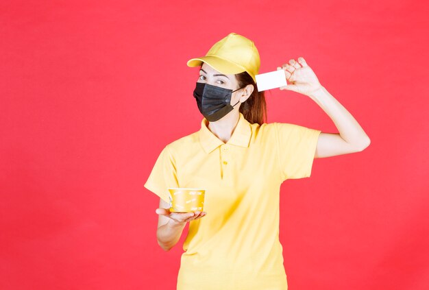 A mensageira de uniforme amarelo e máscara preta está entregando um copo de macarrão e apresentando seu cartão de visita