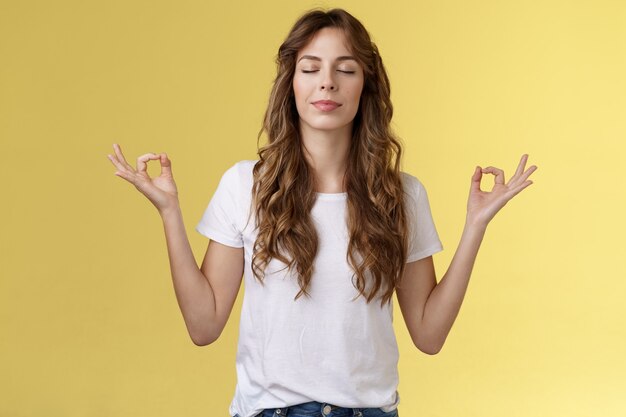 A mente vagueia pelos problemas. Menina om cantando meditação feche os olhos sorrindo encantado encontrado paz relaxamento sentindo aliviado respiração prática budista mãos para os lados mudra lótus pose fazer ioga.