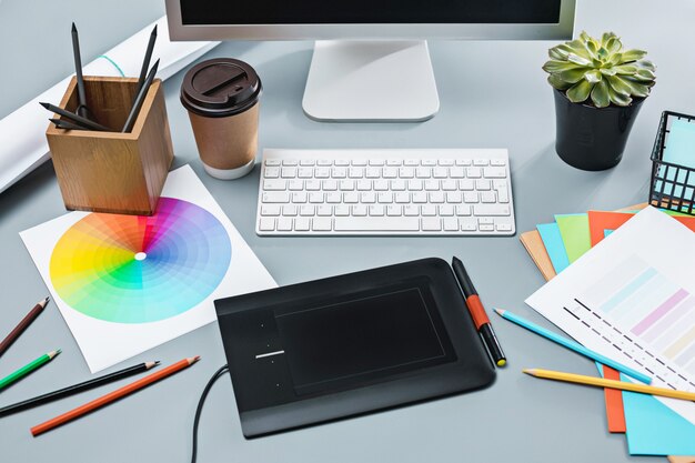 A mesa cinza com laptop, bloco de notas com uma folha em branco, vaso de flores, caneta e tablet para retoque