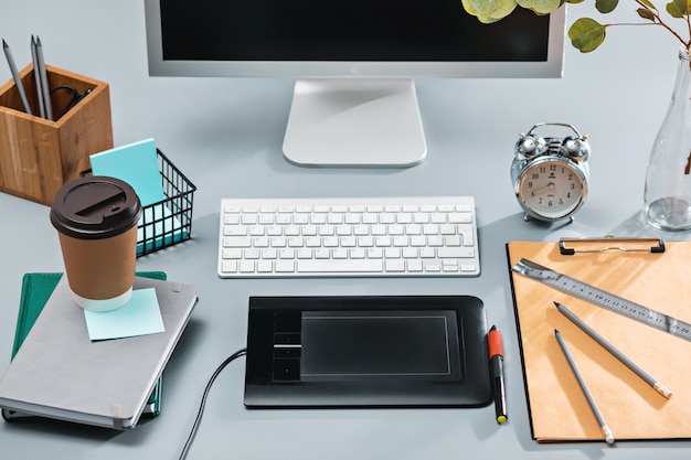 A mesa cinza com laptop, bloco de notas com uma folha em branco, vaso de flores, caneta e tablet para retoque