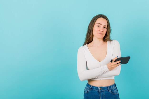 A moça está cruzando os braços segurando o smartphone no fundo azul