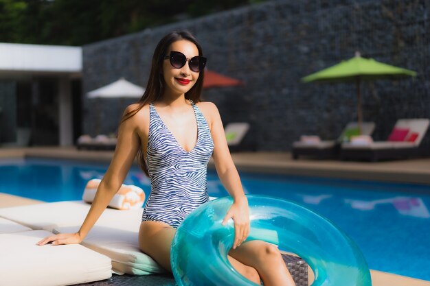 A mulher asiática bonita do retrato relaxa o sorriso feliz em torno da piscina exterior