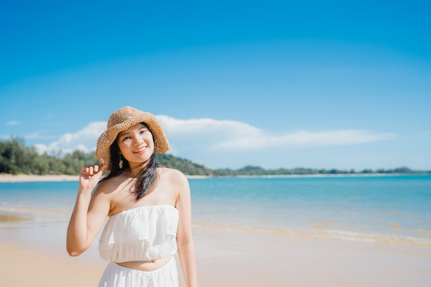 A mulher asiática nova bonita feliz relaxa o passeio na praia perto do mar.