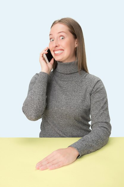 A mulher de negócios feliz sentado com o celular contra um fundo rosa.