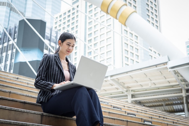 A mulher de negócios que usa laptop fica nos degraus. Conceito de pessoas de negócios.