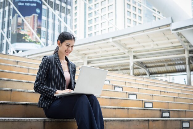 A mulher de negócios que usa laptop fica nos degraus. Conceito de pessoas de negócios.