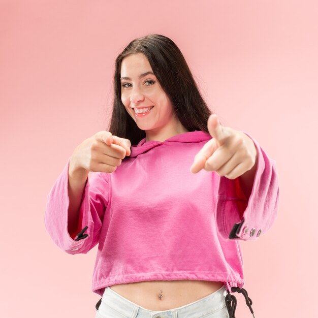 A mulher de negócios sorridente apontar você, quero você, retrato de closeup de metade do comprimento na parede rosa. As emoções humanas, o conceito de expressão facial.