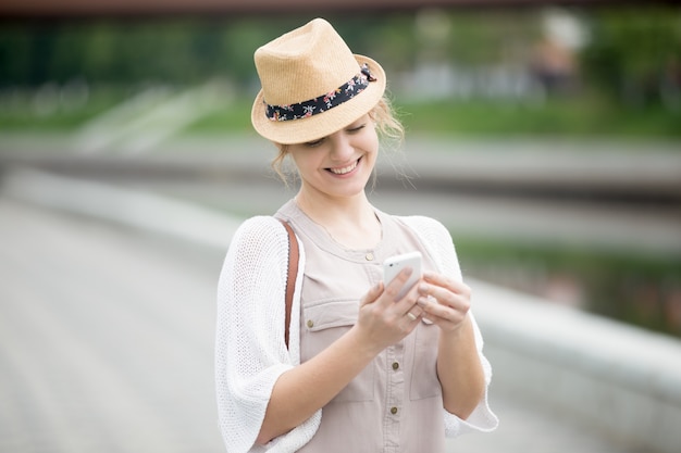 A mulher de sorriso com chapéu olhando para o celular